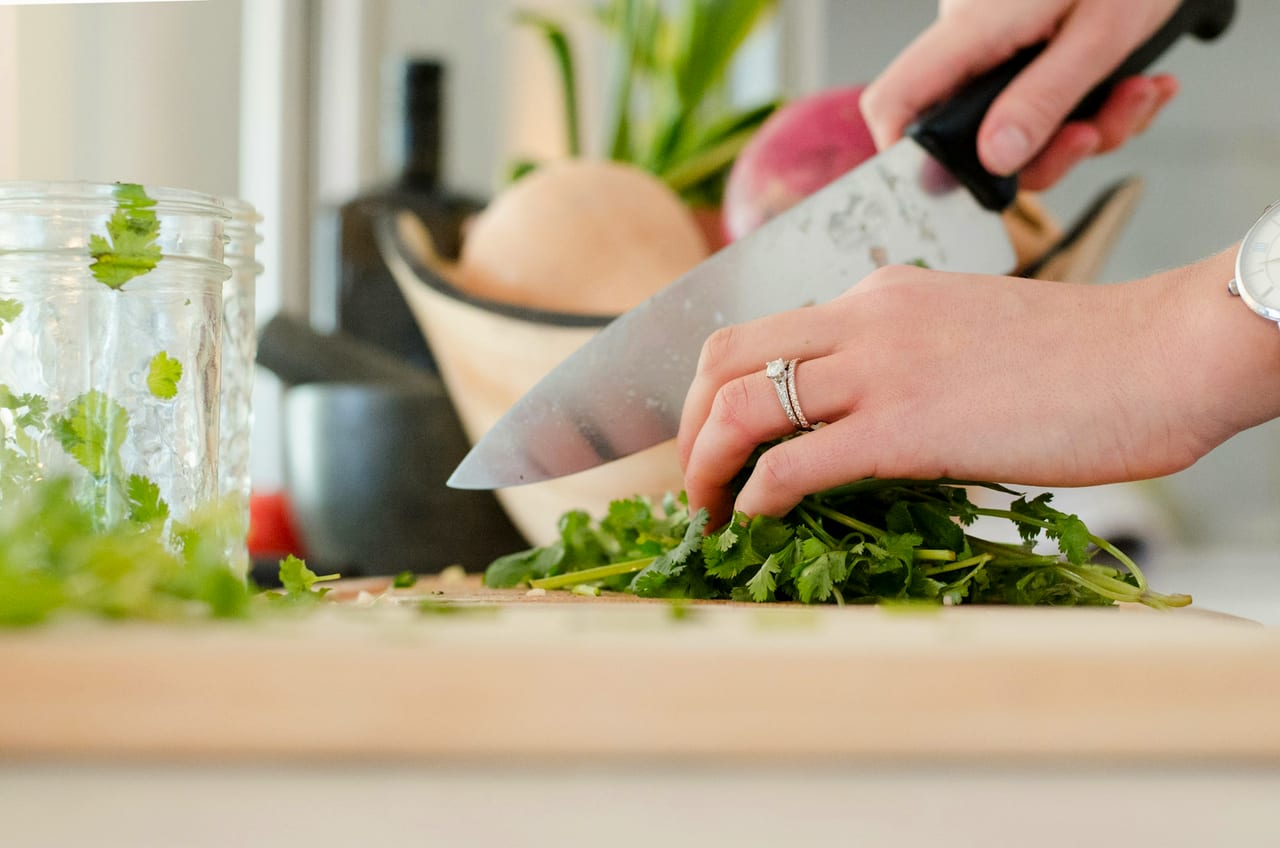Hands cutting vegetables with a knife on a board.