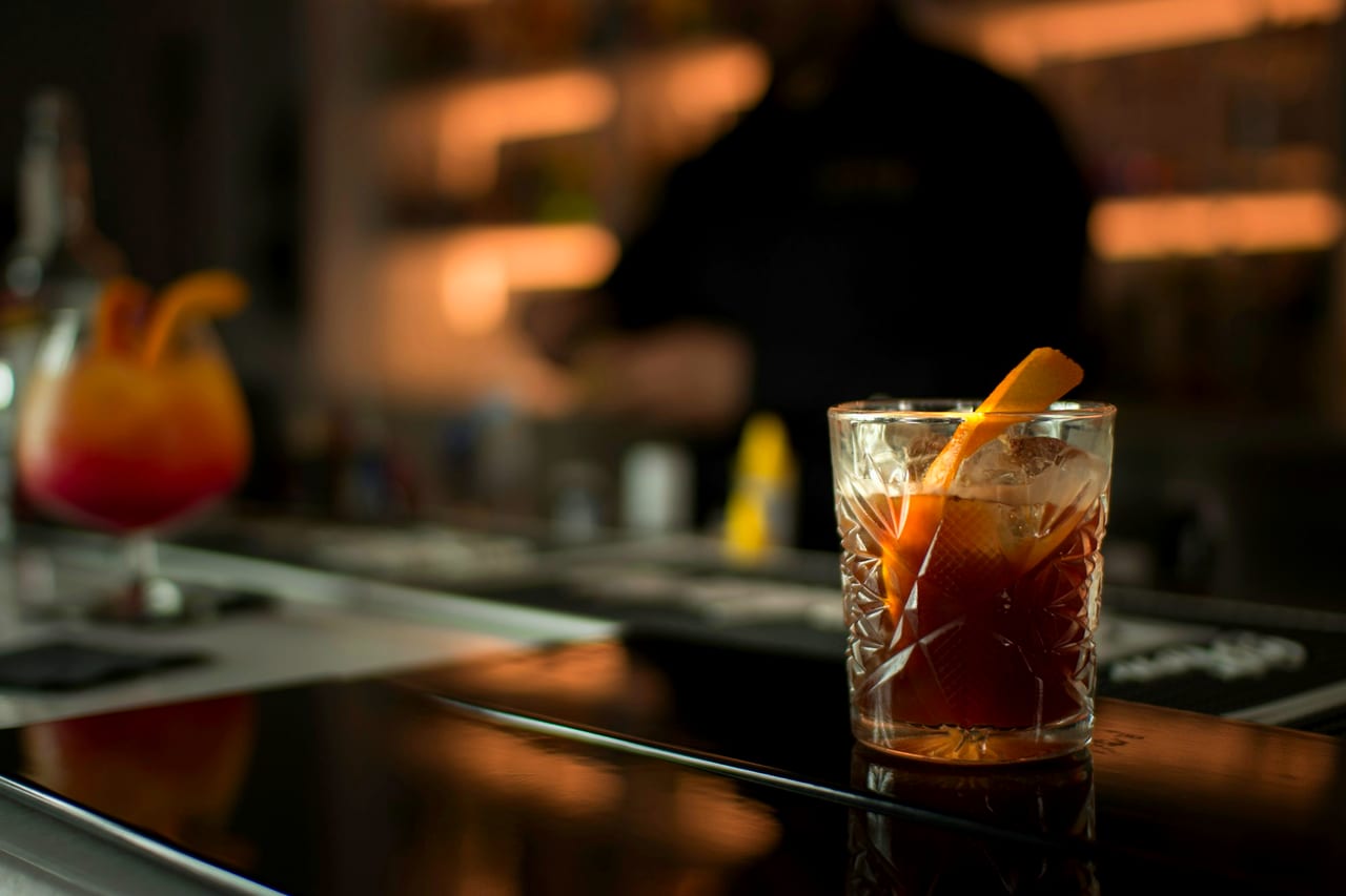 A finished cocktail with an orange peel on a bar counter.
