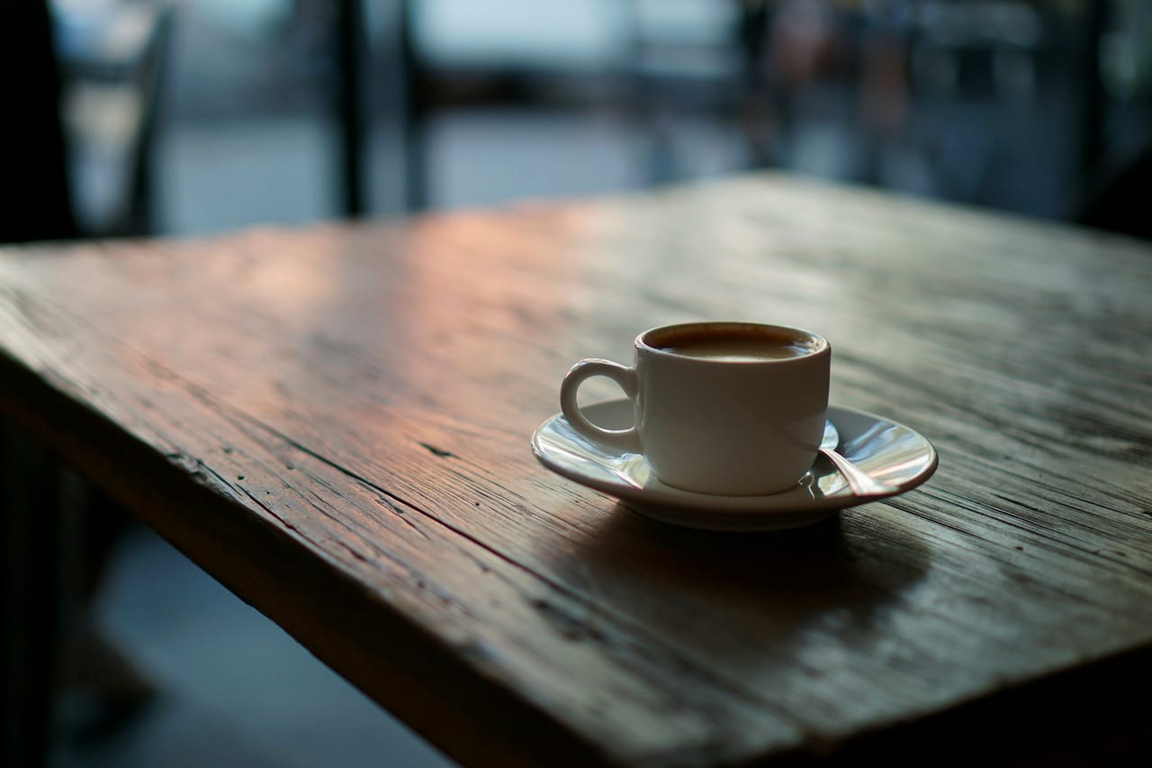 A ceramic cup of coffee on a saucer on a wooden table.