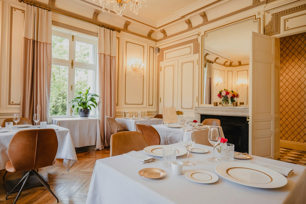 A dining room with tables, chairs and a fireplace.