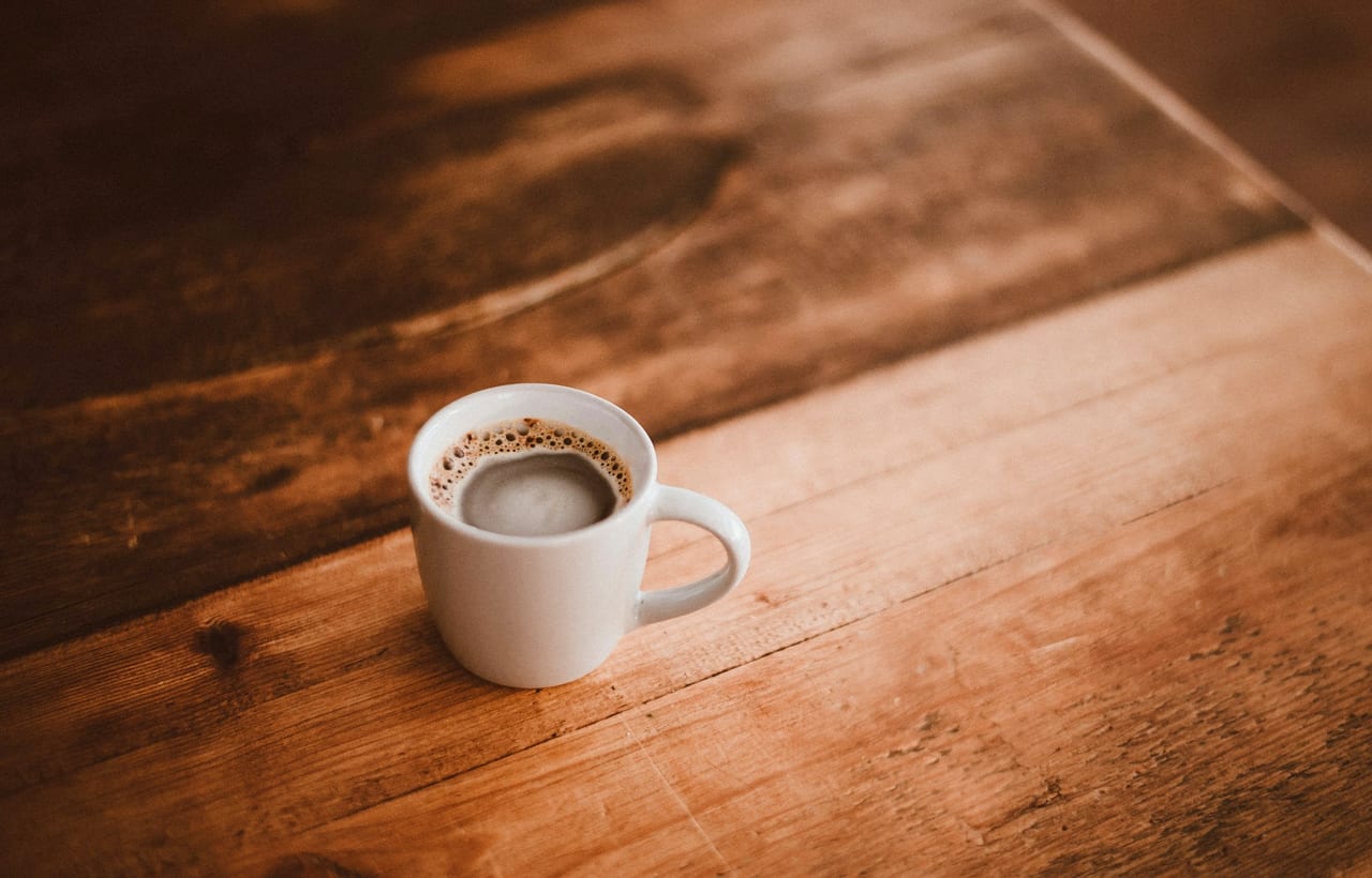 A plain white mug of coffee on a wooden table