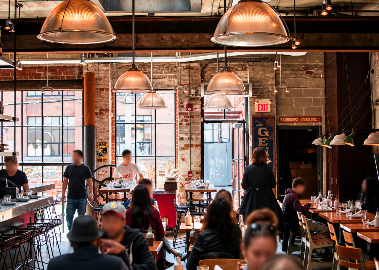 A busy industrial-style restaurant at service — exposed brick, warm pendant lights and full tables