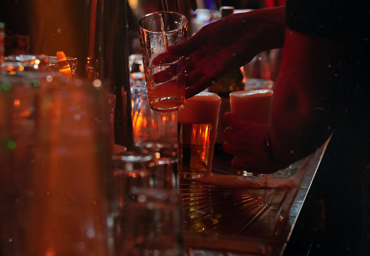 A bartender's hand pouring a fresh beer beside two full glasses on a warmly lit bar