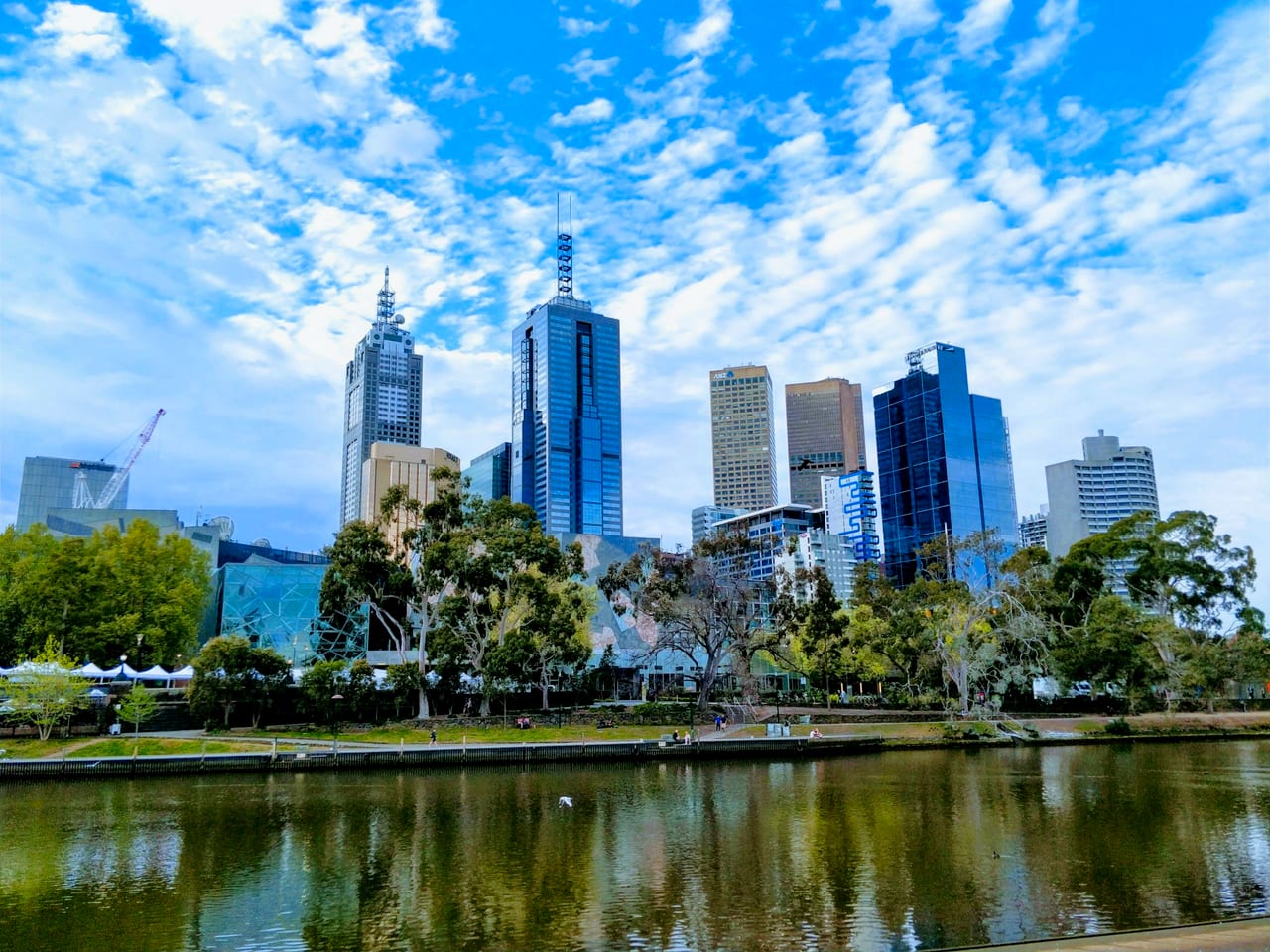 The Melbourne city skyline across the Yarra River, framed by parkland.
