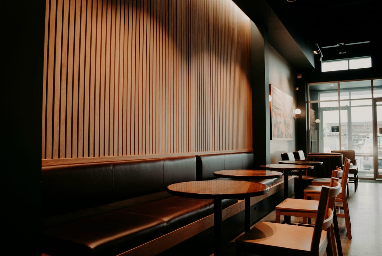 A warm restaurant interior — round timber tables by a leather banquette.