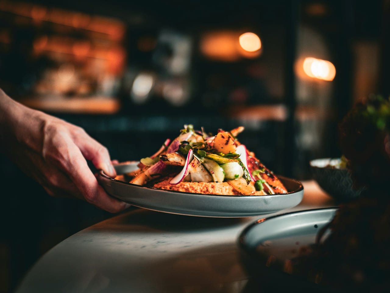 Hands serving a plated dish to a table.