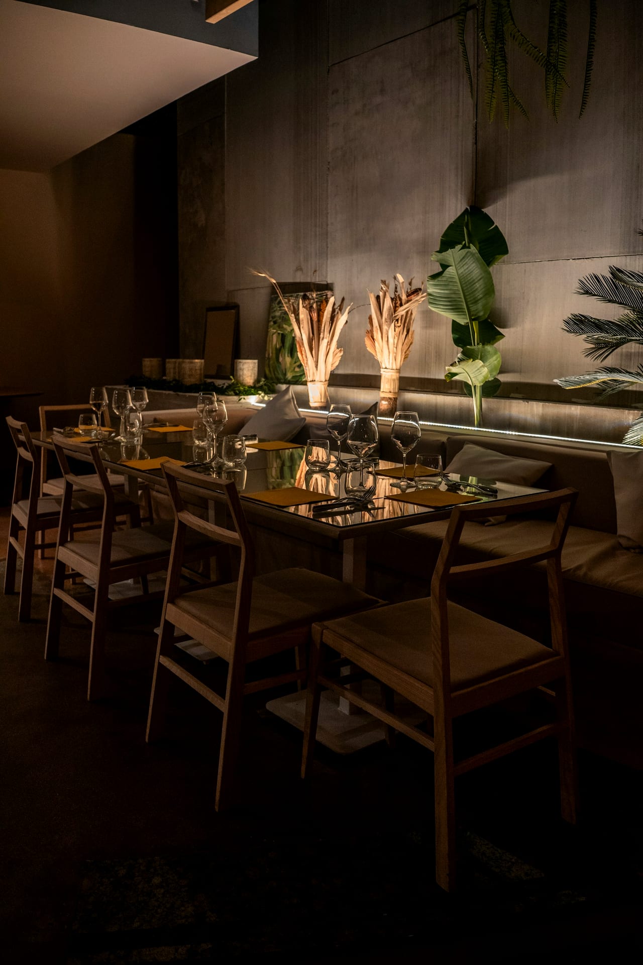 A dim dining room — glasses and place settings laid along a banquette table, ready for service.