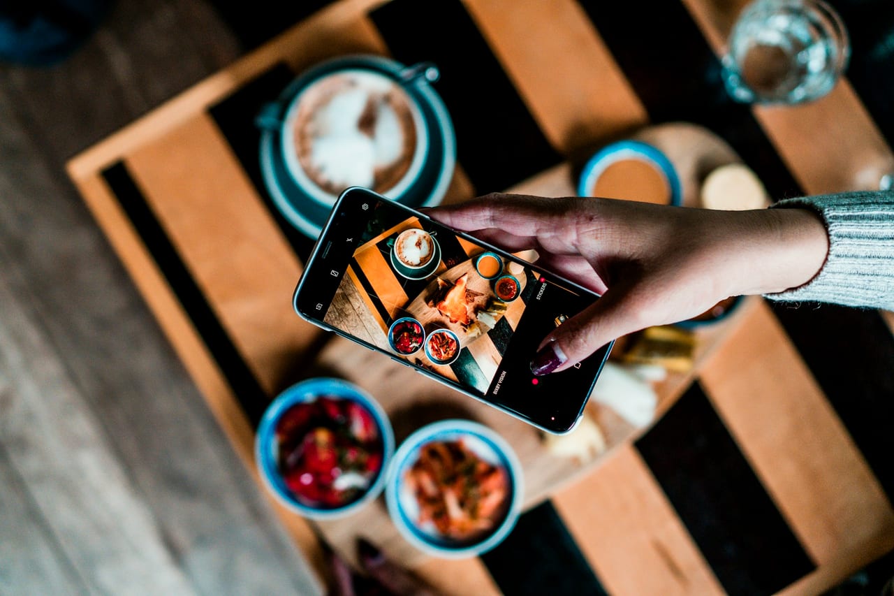 Hands holding a phone over a table of food and drinks