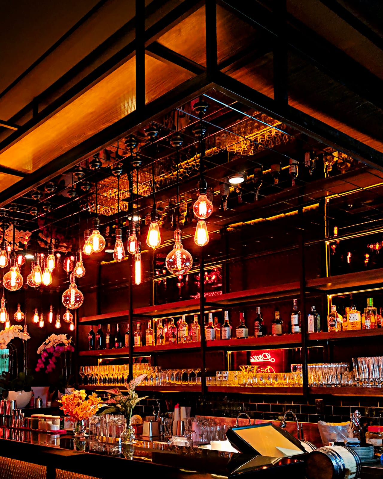 A bar mid-service, glassware and spirits lit under filament bulbs