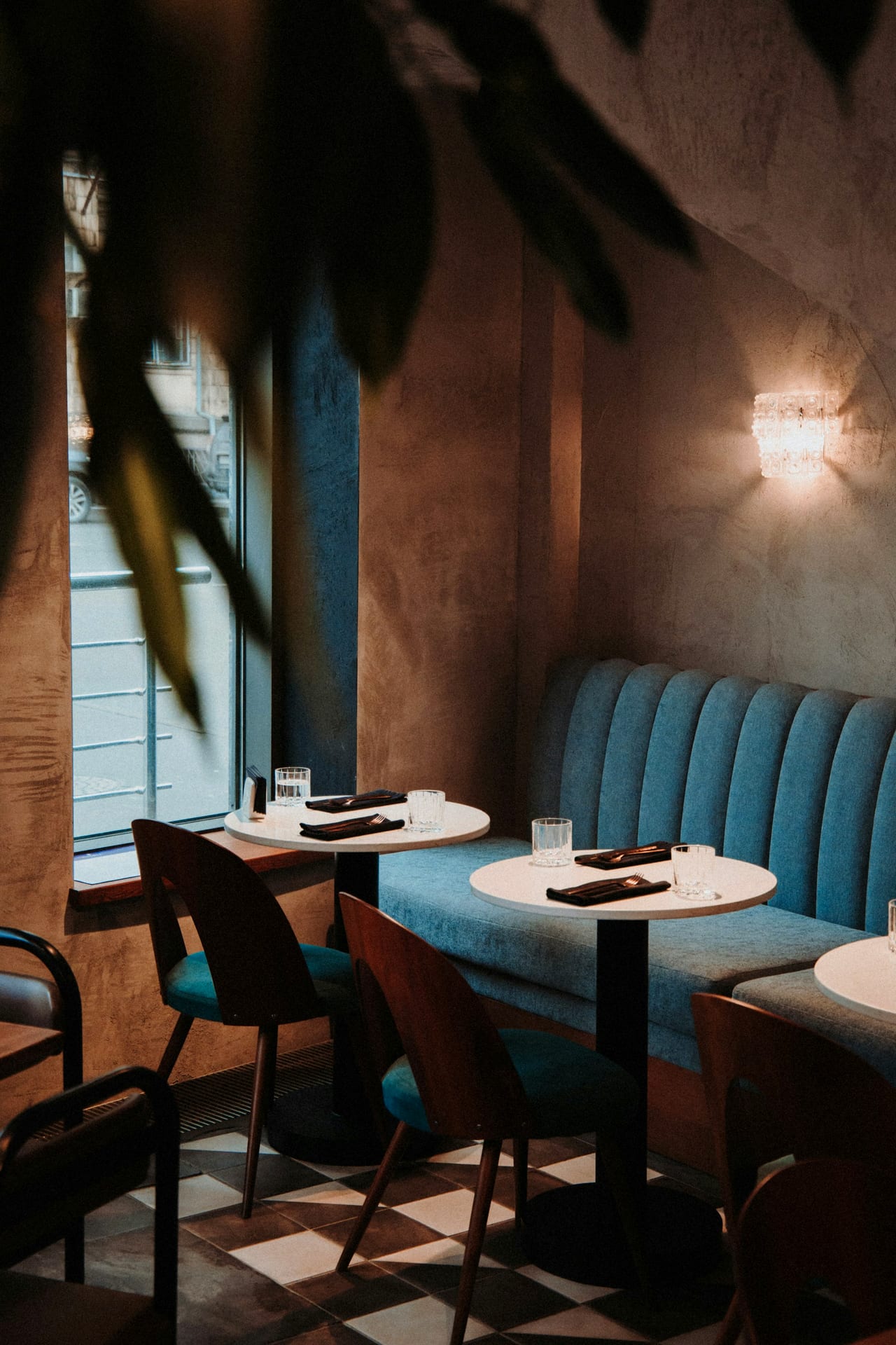 A blue velvet banquette and marble tables laid for service