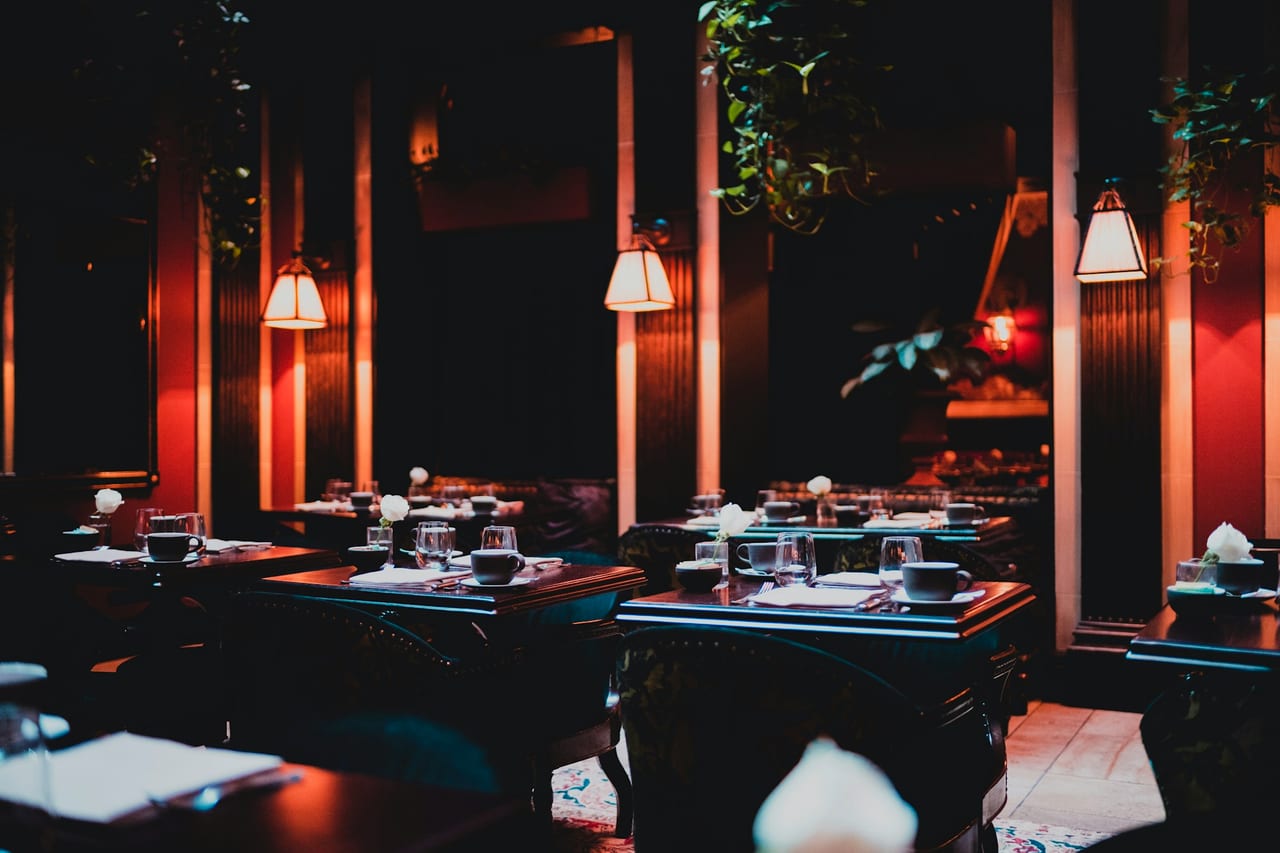 A traditional dining room under low pendant lamps, tables set, unhurried between services