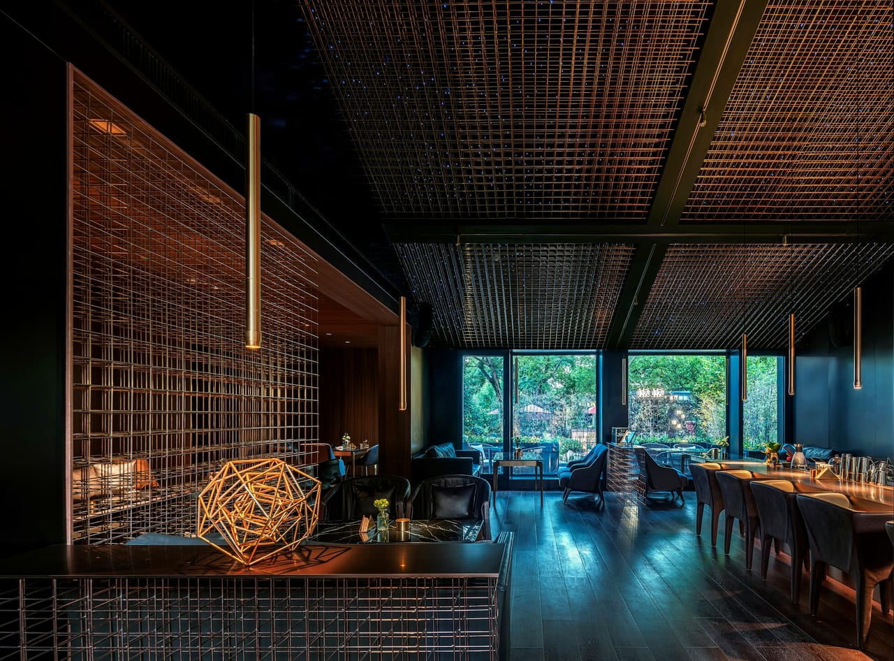A dark, modern dining room with a copper lattice screen and windows onto greenery