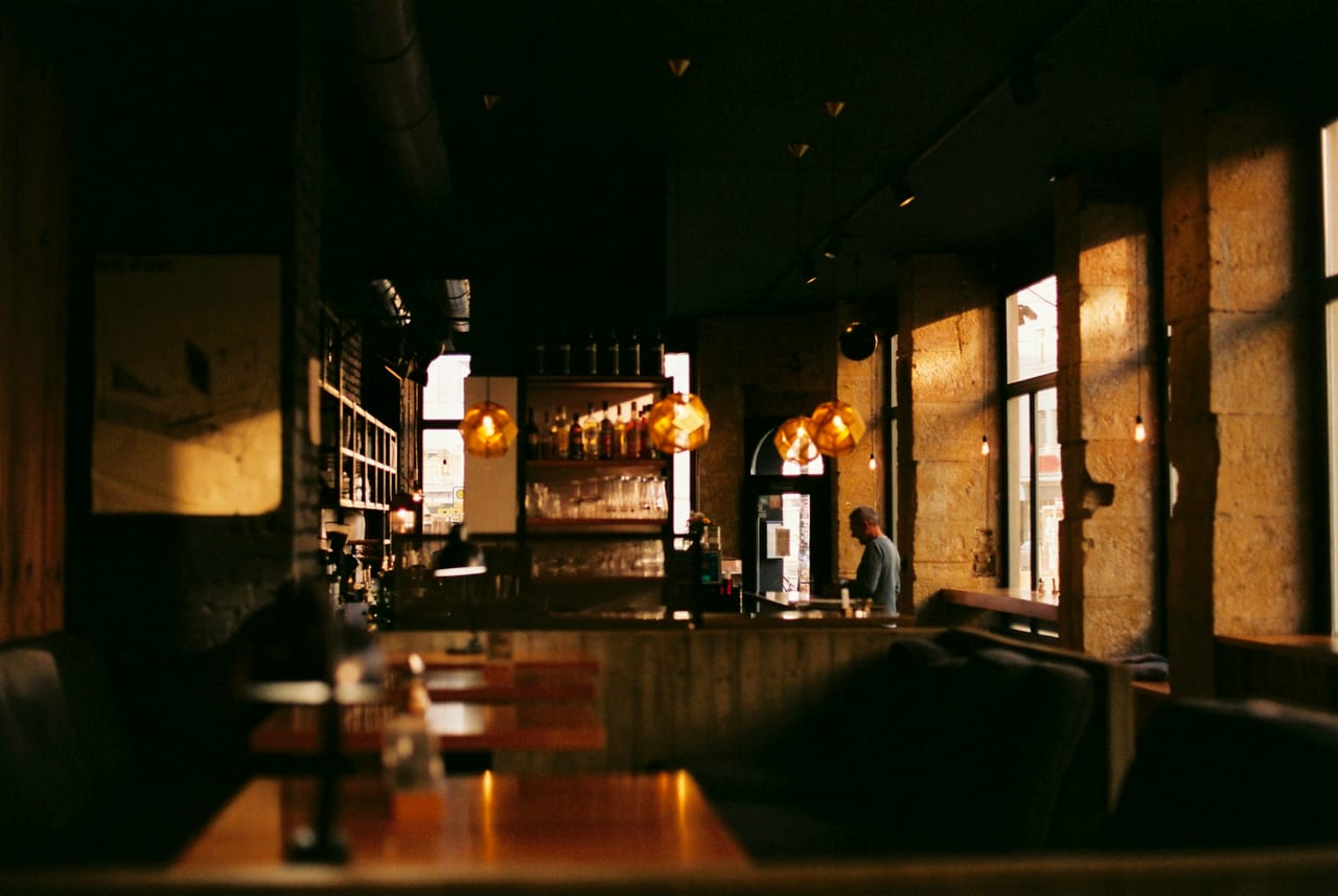 A softly lit London bar and dining room, warm lamps glowing over the counter