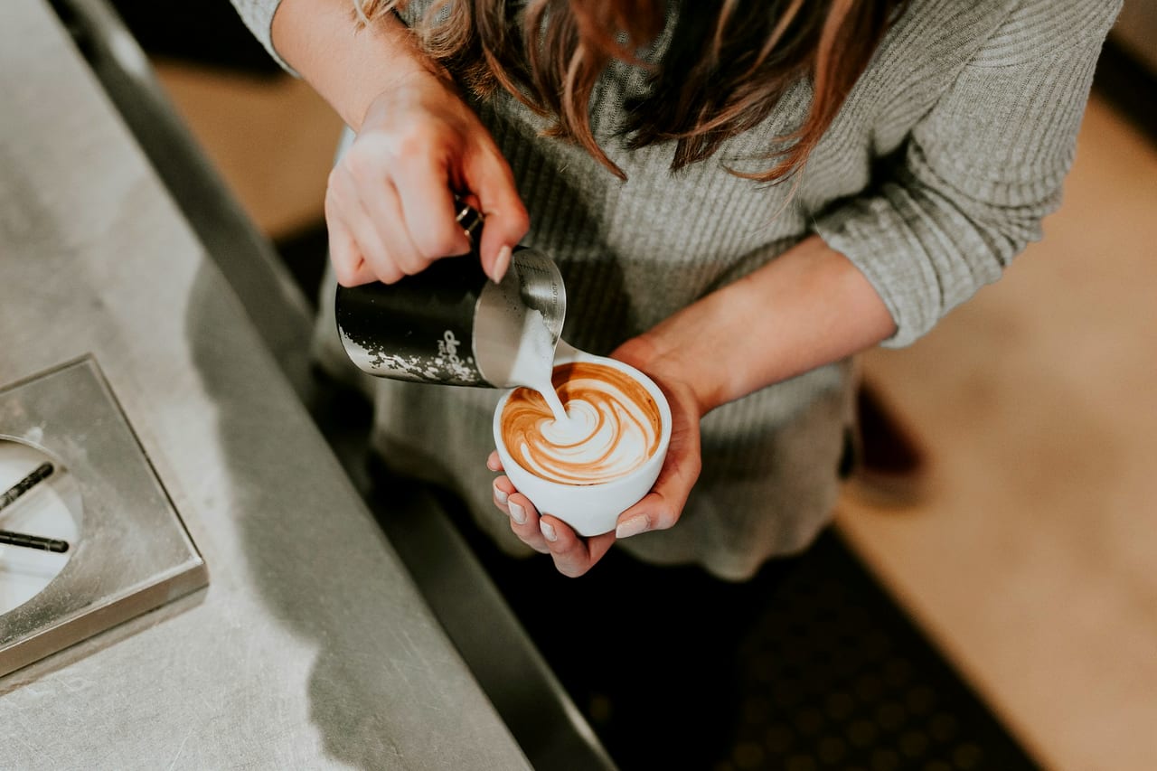 A barista pouring latte art into a white cup held over a café counter