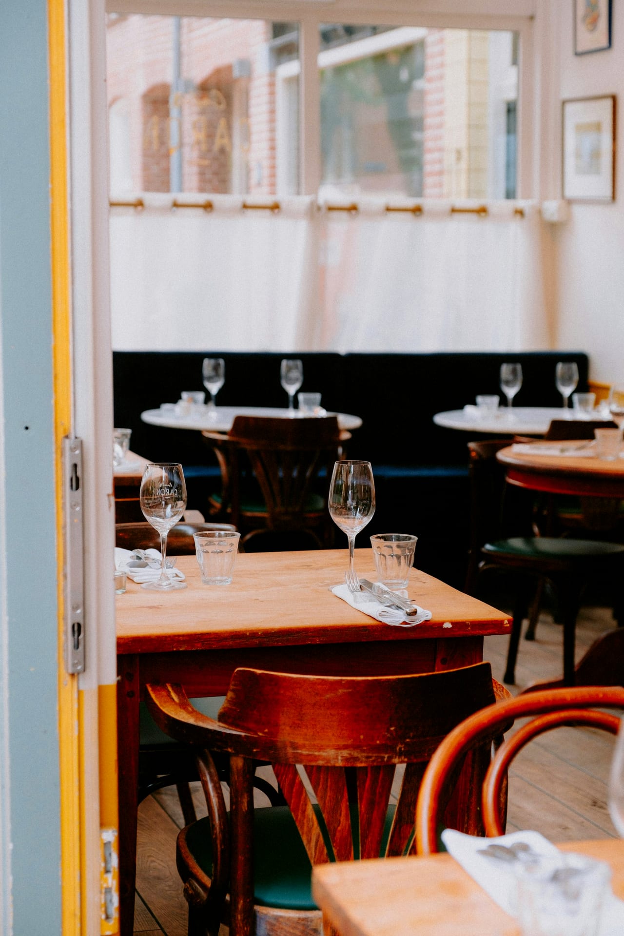 Salle d'un bistrot lyonnais, chaises en bois courbé et tables dressées près de la fenêtre