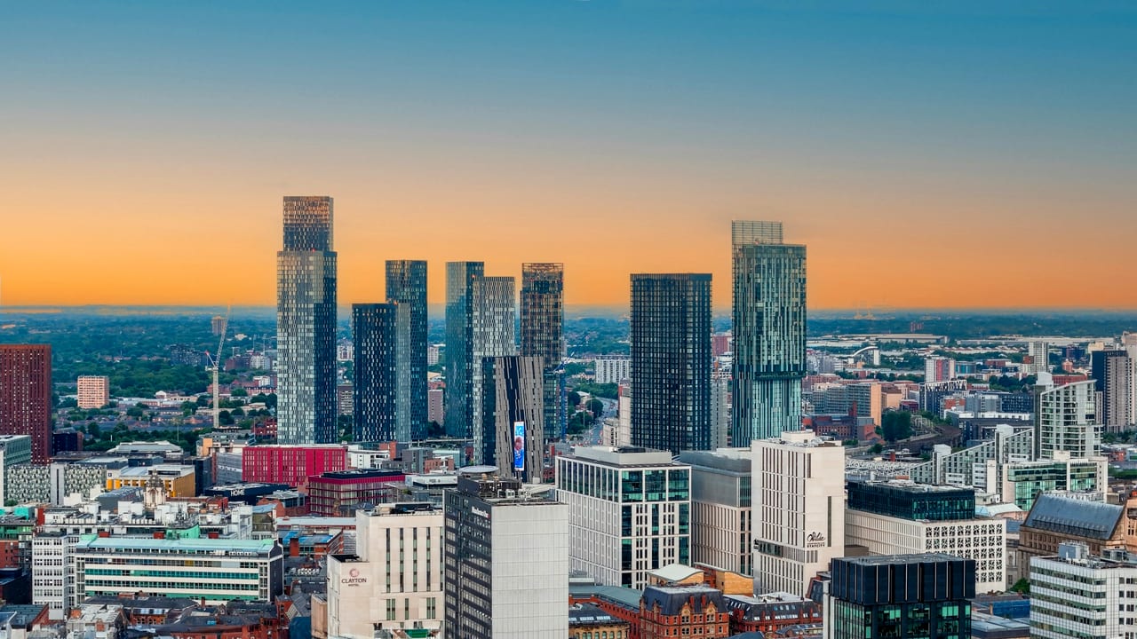Manchester skyline at golden hour, glass towers rising above the city