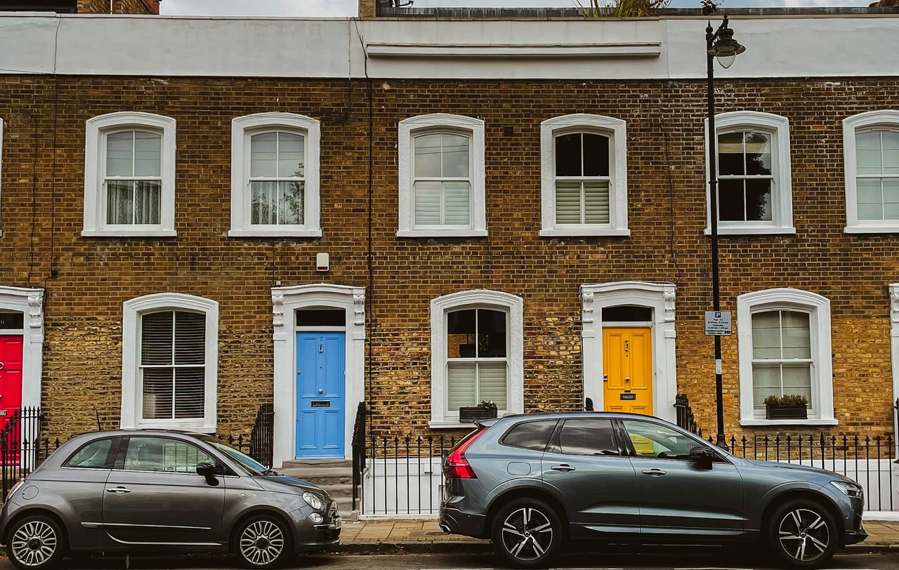 A brick Georgian terrace with blue and yellow front doors and two parked cars